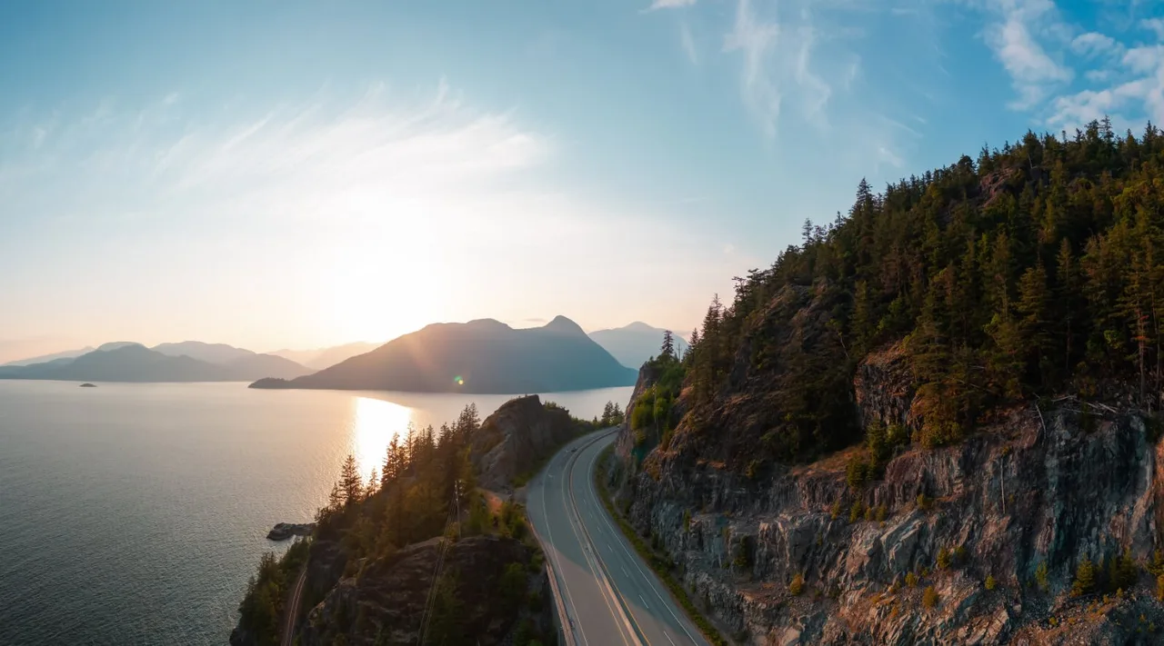 Sea to Sky Highway winding between forested cliffs and Howe Sound at sunset
